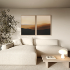 A minimalist living room with a cream sofa, small wooden coffee table holding a lamp and book, two Sienna Echo Set of 2 wall art pieces above, and a leafy plant in the corner.