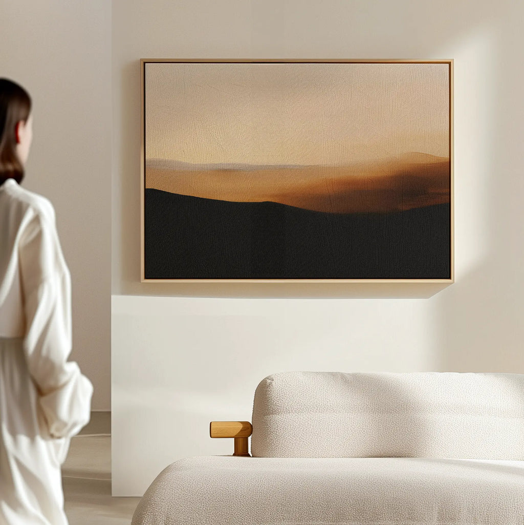 A person stands in a softly lit, minimalist room, admiring the Sienna Ridge Canvas Art in warm brown and beige tones hanging above a light-colored sofa—an elegant touch of modern living room decor.
