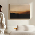 A person stands in a softly lit, minimalist room, admiring the Sienna Ridge Canvas Art in warm brown and beige tones hanging above a light-colored sofa—an elegant touch of modern living room decor.