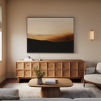 A modern living room features a light sofa, wooden coffee table, textured sideboard, and the Sienna Ridge Canvas Art above. A wall sconce, vase of flowers, and books complete the minimalist decor.