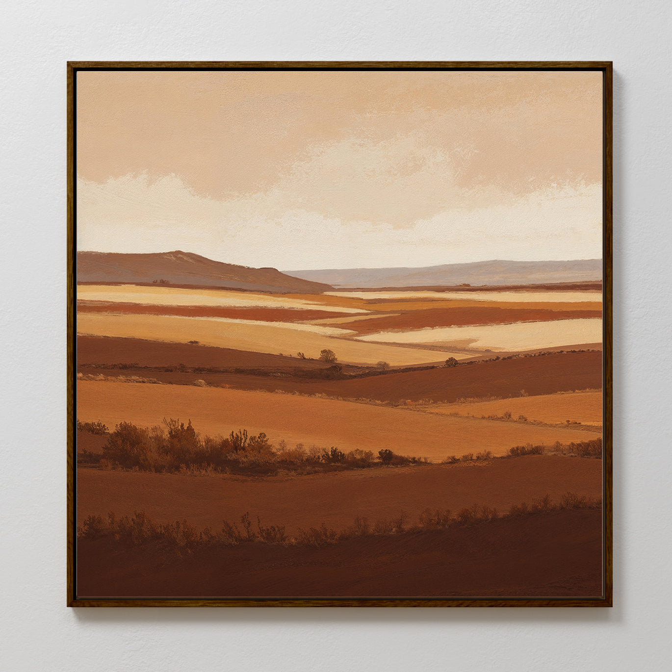 The Sienna Terrain Canvas Art, featuring a terracotta landscape of rolling hills and distant mountains in earthy brown and tan tones beneath a clouded sky, is displayed on a white wall.
