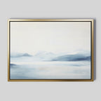 Silent Glaciers Canvas Art features minimalist wall art in a gold frame, showcasing soft blue and gray mountains reflected in tranquil water beneath a pale sky—creating a serene and peaceful atmosphere.