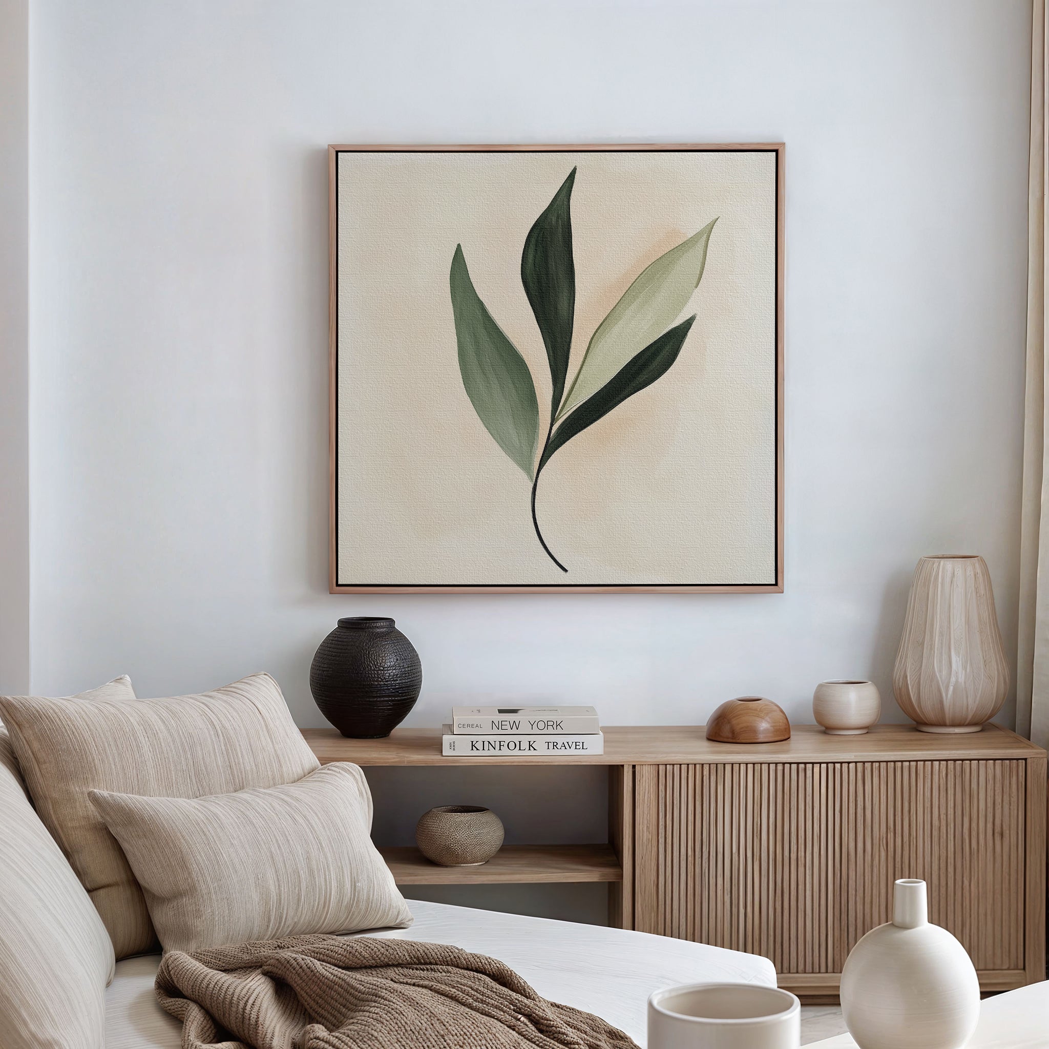 A modern, minimalist living room with a beige couch, neutral cushions, wooden sideboard, decorative vases, books, and the Silent Leaf Canvas Art—botanical wall decor with green leaves that’s perfect for Nordic style fans.