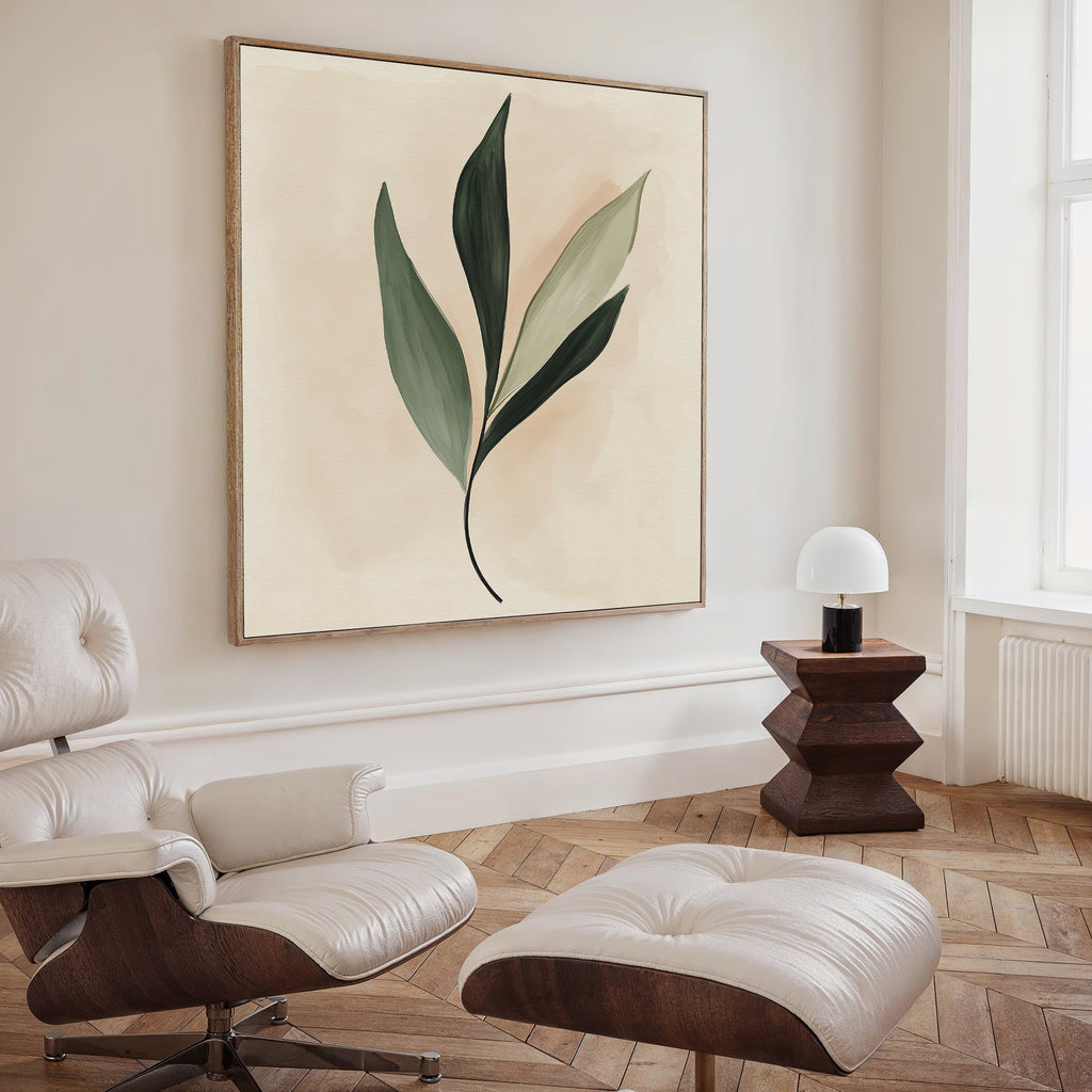 A modern living space featuring a white lounge chair, ottoman, small wooden side table with a white lamp, and the Silent Leaf Canvas Art—a minimalist green leaf wall decor—set against light wood herringbone flooring.