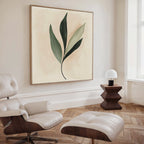 A modern living space featuring a white lounge chair, ottoman, small wooden side table with a white lamp, and the Silent Leaf Canvas Art—a minimalist green leaf wall decor—set against light wood herringbone flooring.