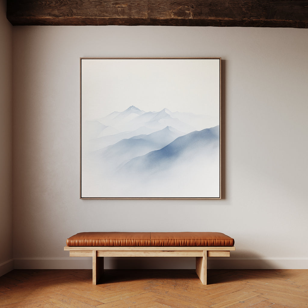 A minimalist room features a wooden bench with a brown leather cushion against a light wall. Above it hangs the Silent Summits Canvas Art—a framed painting of misty blue mountains—perfect for tranquil bedroom decor.