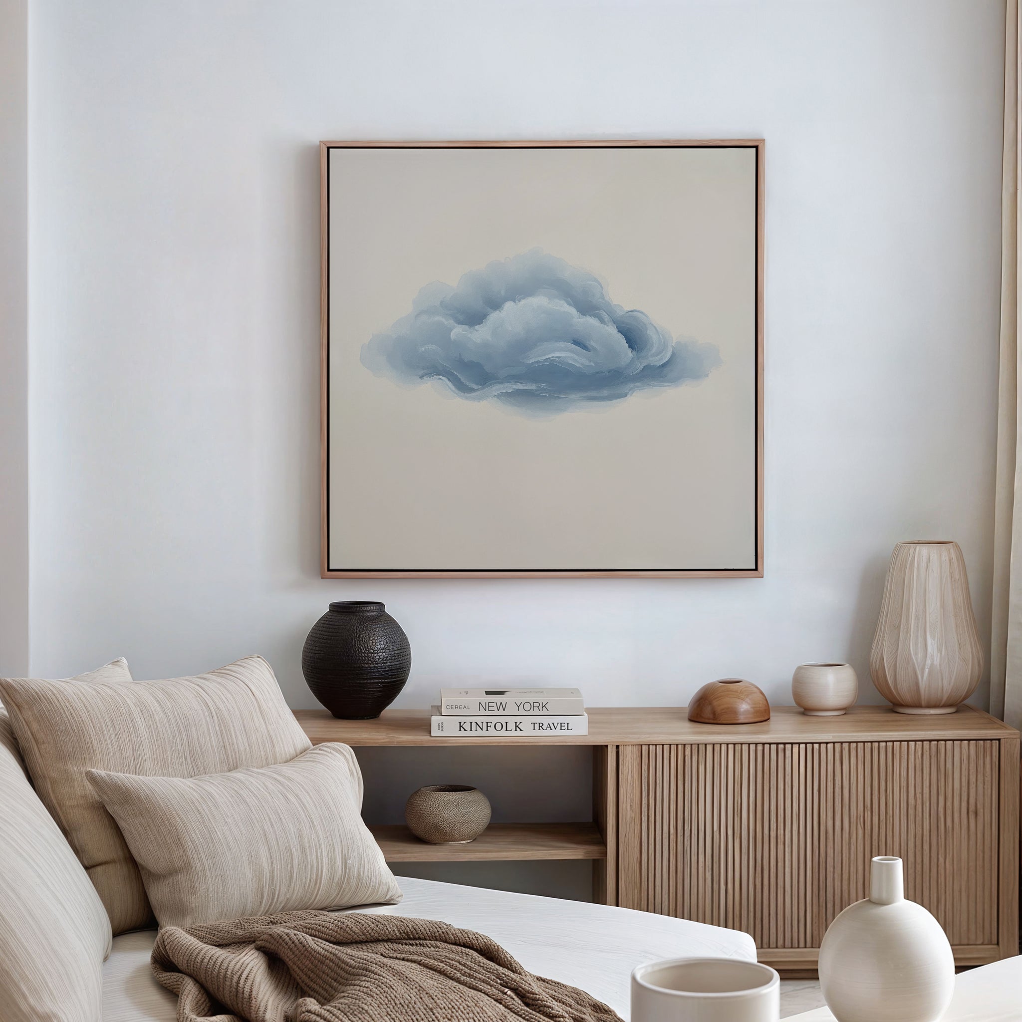 A minimalist living room featuring a beige sofa with cushions, a wooden sideboard holding books and vases, and the Single Cloud Canvas Art as a striking modern decor piece displayed above.