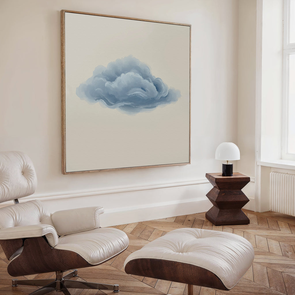 A minimalist living room featuring a white leather chair and ottoman, a small wooden side table with a white lamp, and the Single Cloud Canvas Art on the wall. Light wood floors and cream-colored walls complete the modern decor.