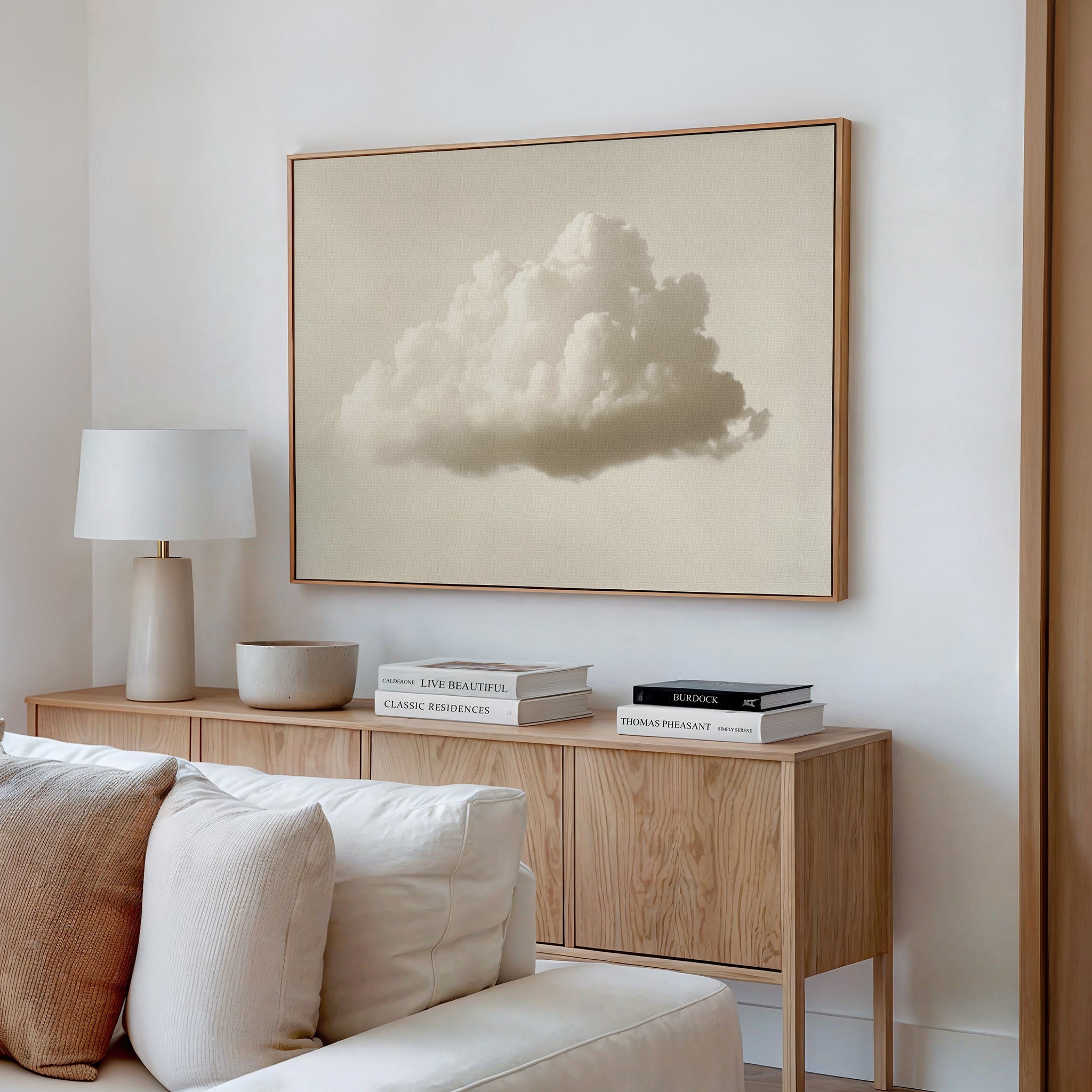 A modern living room features a light wood sideboard with stacked books, a lamp, bowl, and beige couch. Above the sideboard hangs the Singular Vapor Canvas Art – Horizontal, bringing minimalist style to the space.