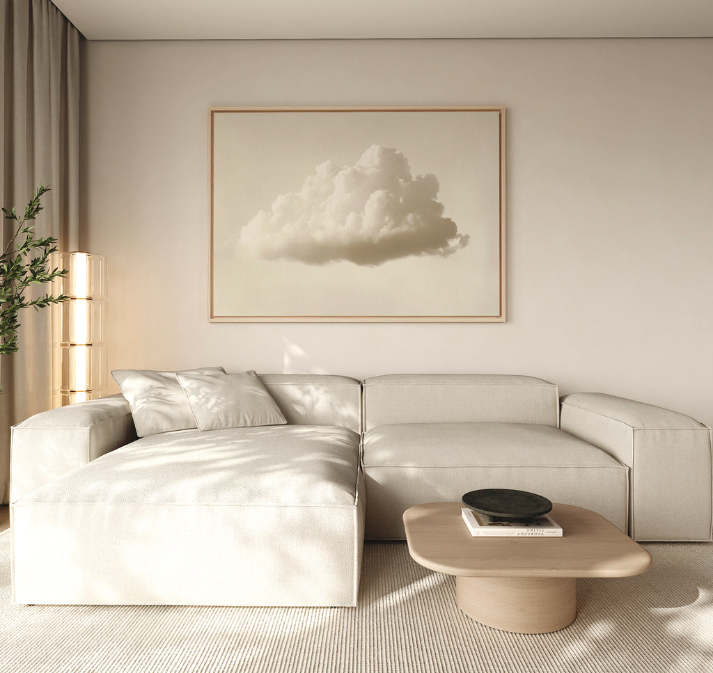 A minimalist living room features a light beige sectional sofa, low wooden coffee table, and modern decor. The Singular Vapor Canvas Art – Horizontal hangs above, while natural light and a potted plant complete the airy space.