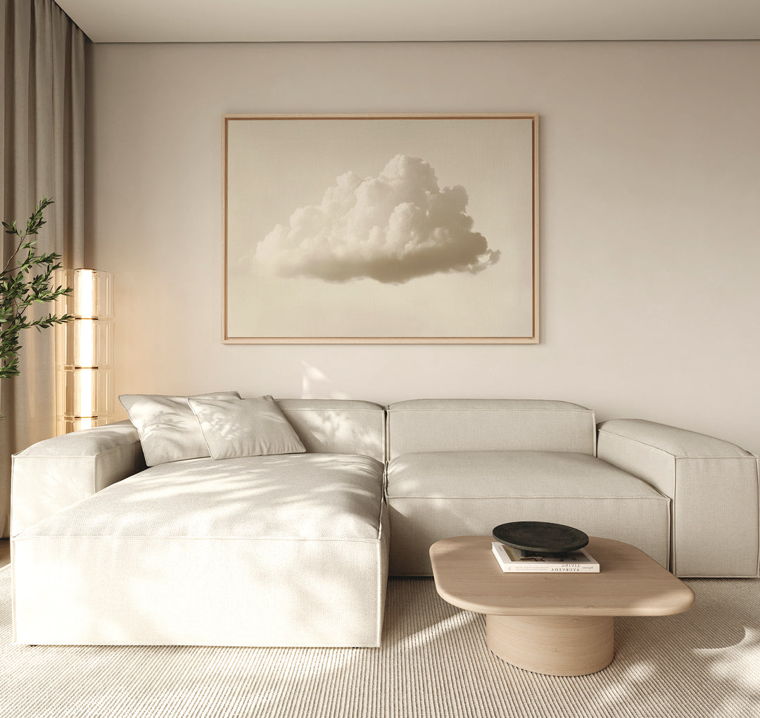 A minimalist living room features a light beige sectional sofa, low wooden coffee table, and modern decor. The Singular Vapor Canvas Art – Horizontal hangs above, while natural light and a potted plant complete the airy space.