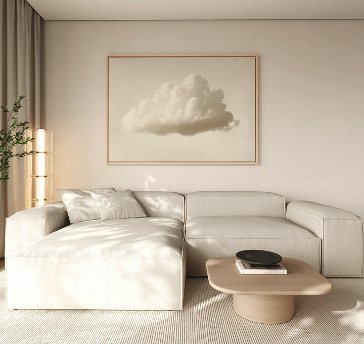 A minimalist living room features a light beige sectional sofa, low wooden coffee table, and modern decor. The Singular Vapor Canvas Art – Horizontal hangs above, while natural light and a potted plant complete the airy space.