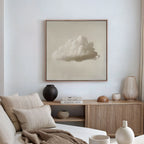 A minimalist living room with neutral tones features a beige sofa, a wooden sideboard with vases and books, and the Singular Vapor Canvas Art—a large cloud-themed piece—bathing in warm natural light for a modern aesthetic.