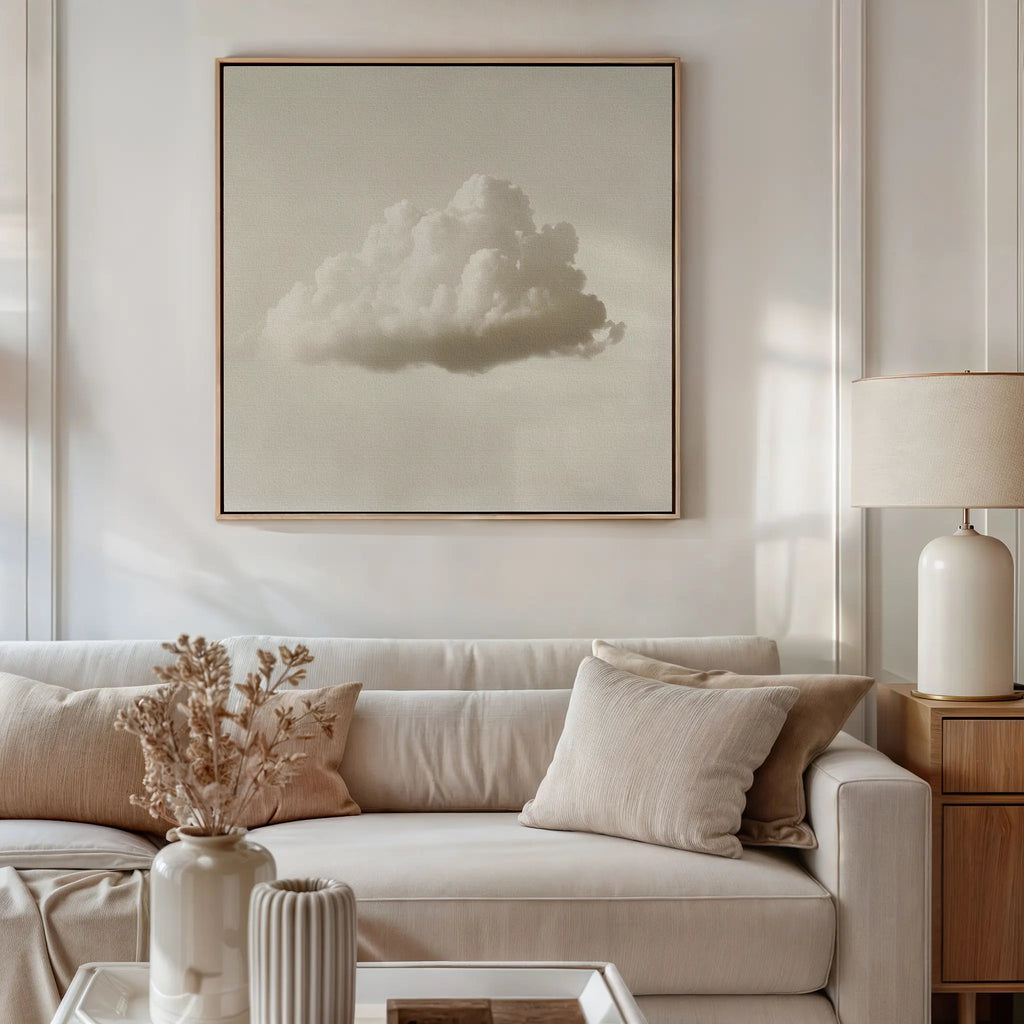 A neutral-toned living room features a white sofa, beige cushions, a lamp, dried flowers in a vase, and minimalist wall art—Singular Vapor Canvas Art—a large framed painting of a single cloud displayed above the sofa for modern flair.