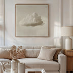 A neutral-toned living room features a white sofa, beige cushions, a lamp, dried flowers in a vase, and minimalist wall art—Singular Vapor Canvas Art—a large framed painting of a single cloud displayed above the sofa for modern flair.