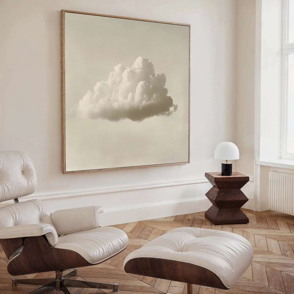 A minimalist living room features a white lounge chair and ottoman, a geometric wood side table with a white lamp, and the Singular Vapor Canvas Art. Light herringbone floors and ample natural light complete the modern space.