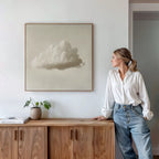 A woman in a white blouse and jeans leans against a wooden cabinet, gazing at the Singular Vapor Canvas Art above her. A small plant and books add subtle style, creating a calm, modern scene ideal for contemporary interiors.
