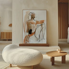 A modern living room features a textured white sofa, a small wooden table with a heart-shaped decor, and the Sitting Silhouette Abstract Canvas Art—a large neutral-toned painting of a seated figure—leaning against the wall.