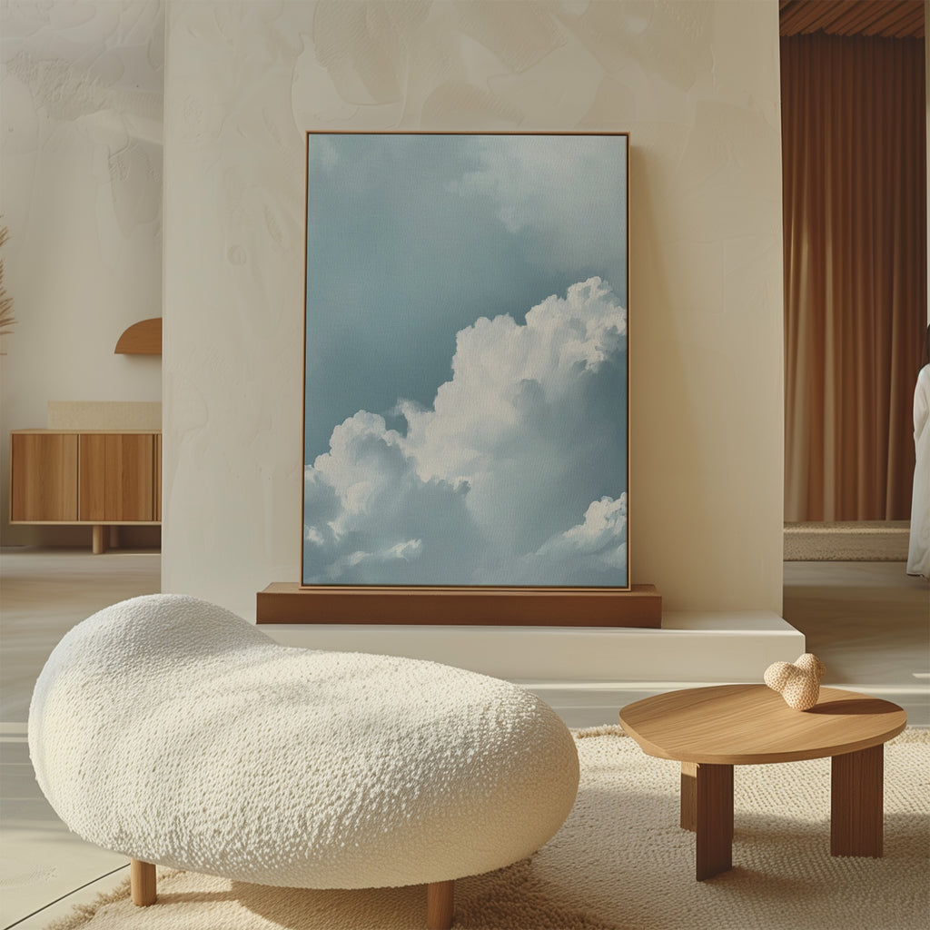 A modern living room featuring a soft, textured white lounge chair, a small wooden table with heart-shaped decor, and Sky Serenade Abstract Canvas Art—a large painting of fluffy white clouds against a blue sky—resting on the floor.