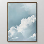 Sky Serenade Abstract Canvas Art features fluffy white clouds on a soft blue sky, framed and displayed on a plain white wall—minimalist wall art that brings calming, serene vibes to any living room decor.