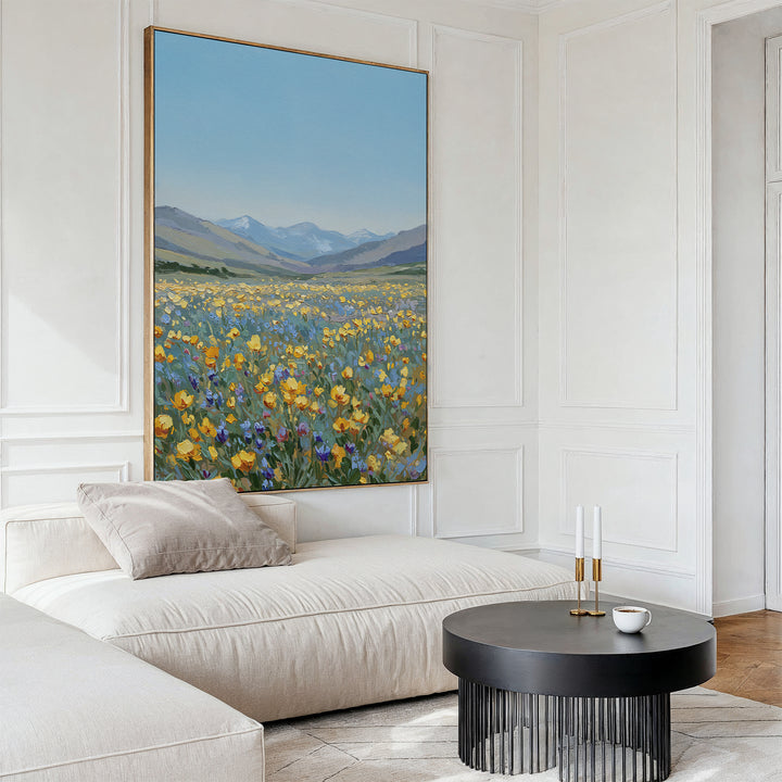A bright living room features Skyview Field Canvas Art above a cream sectional sofa, accented with pillows, a round black coffee table, two white candles, and a cup on a saucer for a modern decor touch.