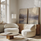 A modern living room with two white rounded armchairs, a wooden coffee table, and the Smoky Peaks Set of 2 landscape wall art on a wooden sideboard against a light wall, all brightened by large windows.
