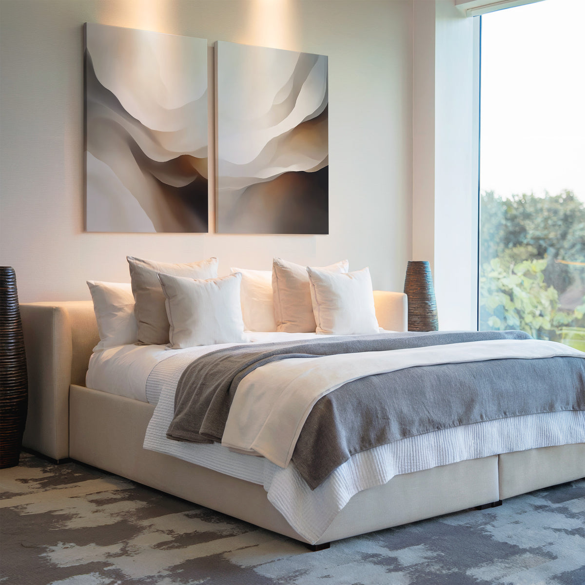 A modern bedroom features a large bed with white and gray bedding, several pillows, striking wall art above the headboard, and the Smooth Flow Set of 2 tall vases on each side, all bathed in natural light for perfect modern home decor.