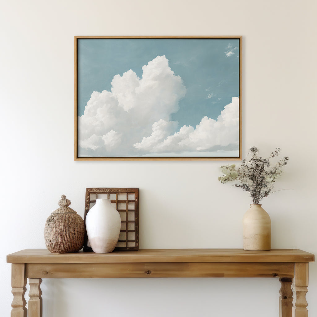 A wooden console table with vintage vases and dried flowers stands against a white wall, beneath the Soaring Peace Canvas Art featuring fluffy white clouds in a serene sky.