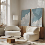 A modern, minimalist living room features the Soaring Peace Set of 2 rounded white chairs, a low wooden coffee table, vintage cloud-themed wall art on a wooden sideboard by tall windows, and cozy natural light flooding the space.