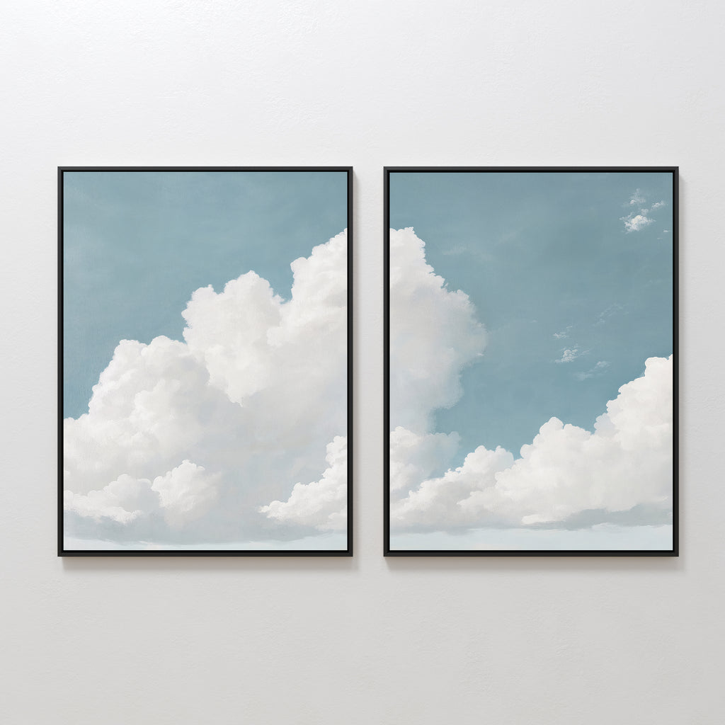 The Soaring Peace Set of 2 features framed wall art prints of white clouds on a blue sky, displayed side by side. The tranquil design flows across both frames for a cohesive, calming effect on any plain white wall.