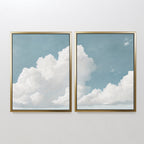 The Soaring Peace Set of 2 features framed prints of fluffy white clouds on a blue sky, hung side by side to create a tranquil, serene atmosphere on any plain wall.