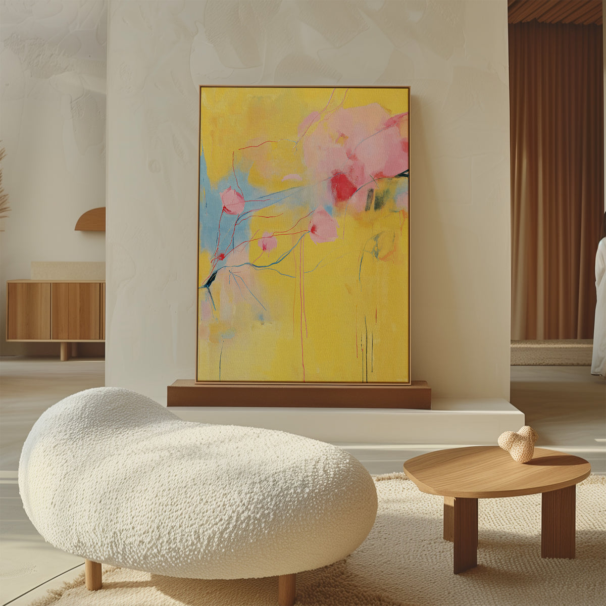 A modern living room features a textured white lounge chair, a small wooden coffee table, and the Soft Bloom Abstract Canvas Art in yellow and pink on a neutral wall, all bathed in warm natural light for an inviting atmosphere.