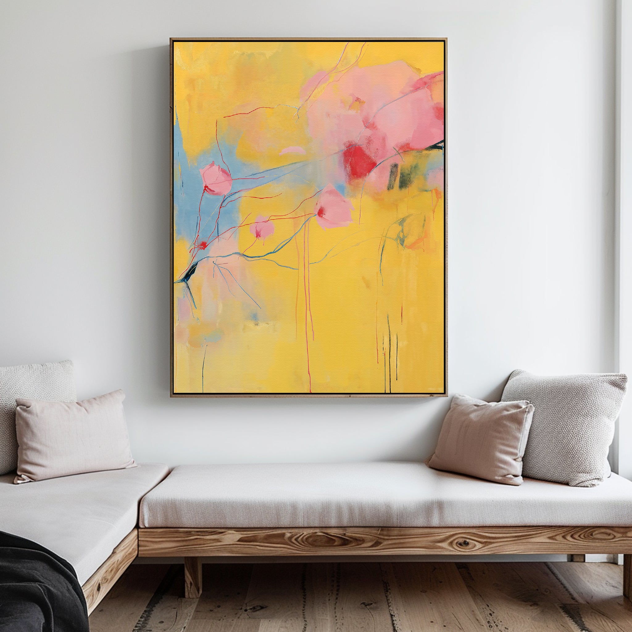 A modern living room with light wood furniture and neutral cushions, featuring the Soft Bloom Abstract Canvas Art—a large, colorful painting in yellow, pink, and blue—hanging on a white wall.