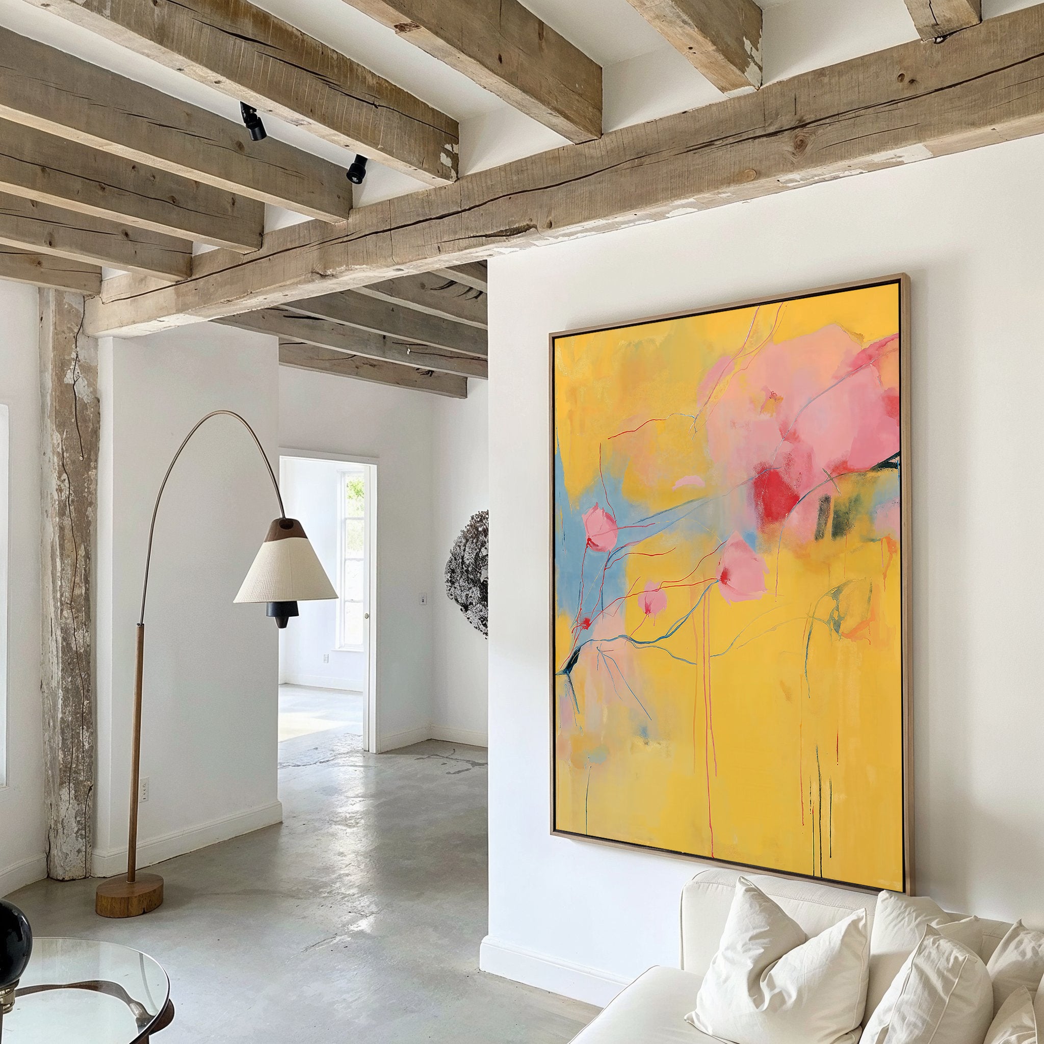 A modern living room with exposed wooden beams, white walls, a floor lamp, and the Soft Bloom Abstract Canvas Art in yellow, pink, and blue above a white sofa—great for creating eye-catching living room decor.