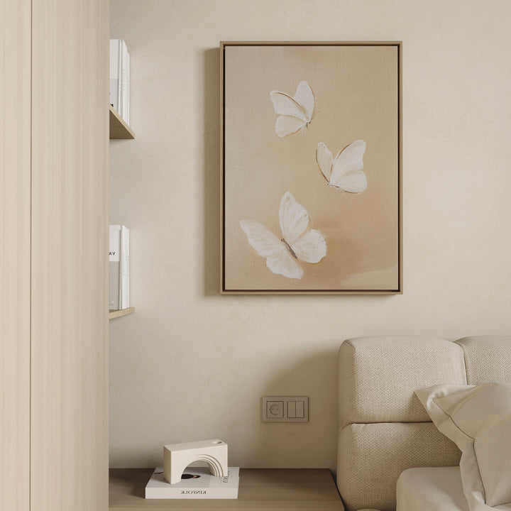 A minimalist living room with beige walls, a soft light-colored sofa, and the Linen Wings Canvas Art above the sofa. Nearby, books rest on shelves with a modern geometric bookend atop a wooden surface, evoking Nordic Park charm.