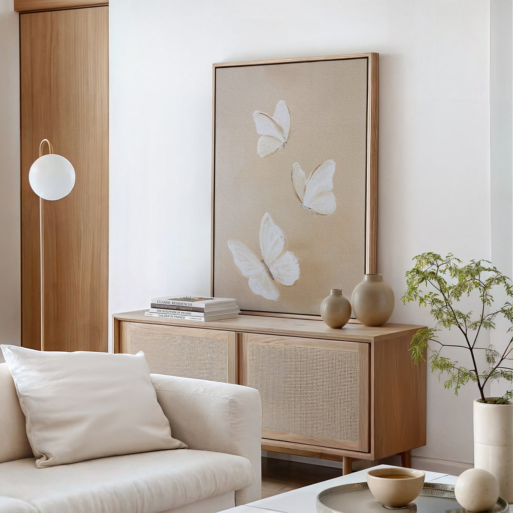 A minimalist living room with a cream sofa, light wood cabinet, neutral-toned vases, the Linen Wings Canvas Art as elegant wall decor, a round white lamp, stacked books, and a small potted plant on the cabinet.