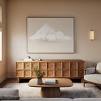 A cozy living room with neutral tones, featuring a wooden sideboard with circular patterns, the Soft Drift Canvas Art above it, a small coffee table with books, a vase of flowers, and a light gray sofa on a textured rug.