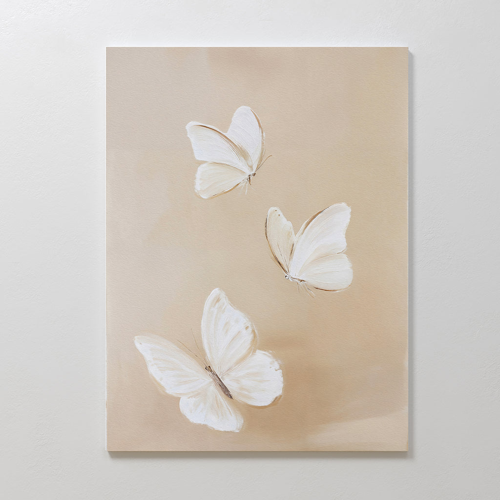 Linen Wings Canvas Art features three white butterflies with delicate wings on a light beige background. Spaced apart at various angles, this elegant piece adds gentle movement and charm to your wall decor.