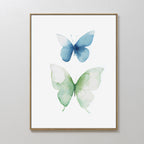 Soft Flight Canvas Art: A Nordic Park-inspired minimalist wall print with two watercolor butterflies, one blue and one green, set against a white background in a slim gold frame.