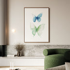 A modern living room with a green curved sofa, low table, and Soft Flight Canvas Art—large framed blue and light green watercolor butterflies—hanging on a neutral wall above a marble shelf.