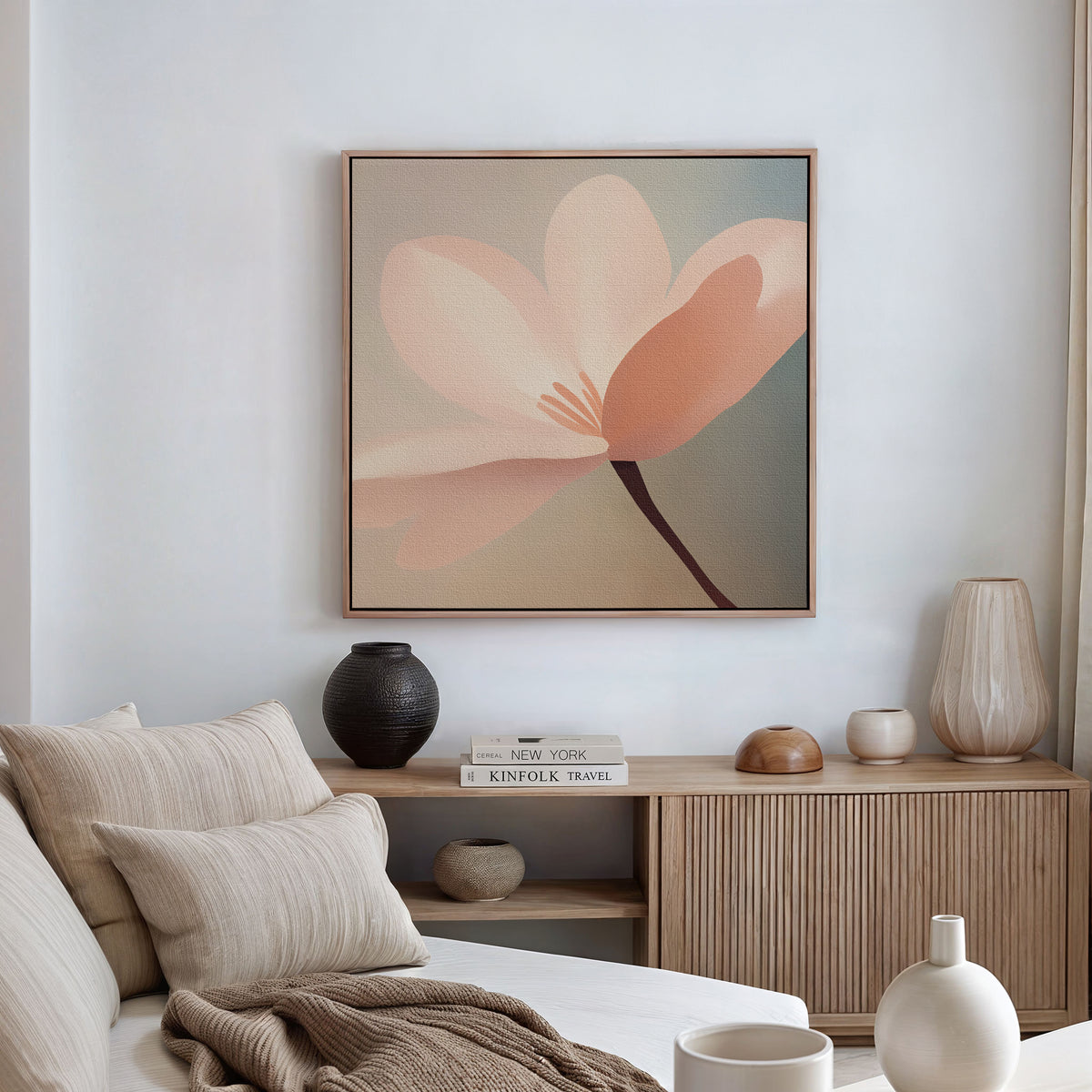 A cozy living room featuring a beige sofa, neutral cushions, and a wooden sideboard. The Soft Pink Glow Canvas Art hangs above, while decorative vases, books, and pottery accent the space bathed in natural light.