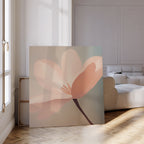 The Soft Pink Glow Canvas Art leans against the wall in a bright, modern living room with parquet floors and a white sofa. Sunlight pours through tall windows, highlighting the elegant minimalist floral design.