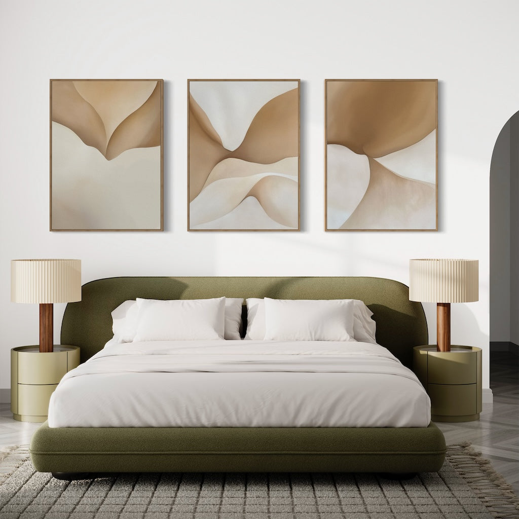 A modern bedroom features a green upholstered bed with white bedding, beige nightstands and lamps, and the Soft Sands Set of 3 abstract beige and brown paintings above the bed. A cozy gray rug completes the serene look.