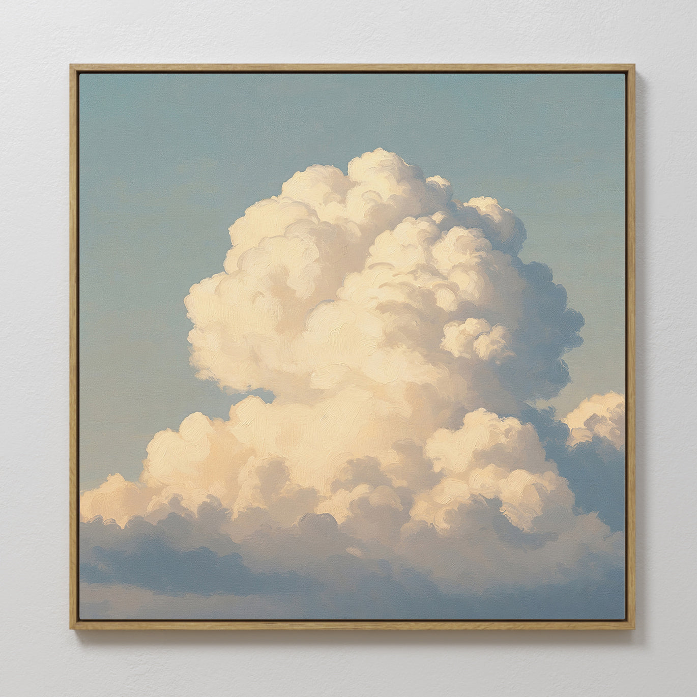 The Soft Skies Rising Canvas Art features a large, fluffy white cloud against a pale blue sky. Framed and hung on a white wall, its soft lighting and golden tones create tranquil, sky-inspired decor.