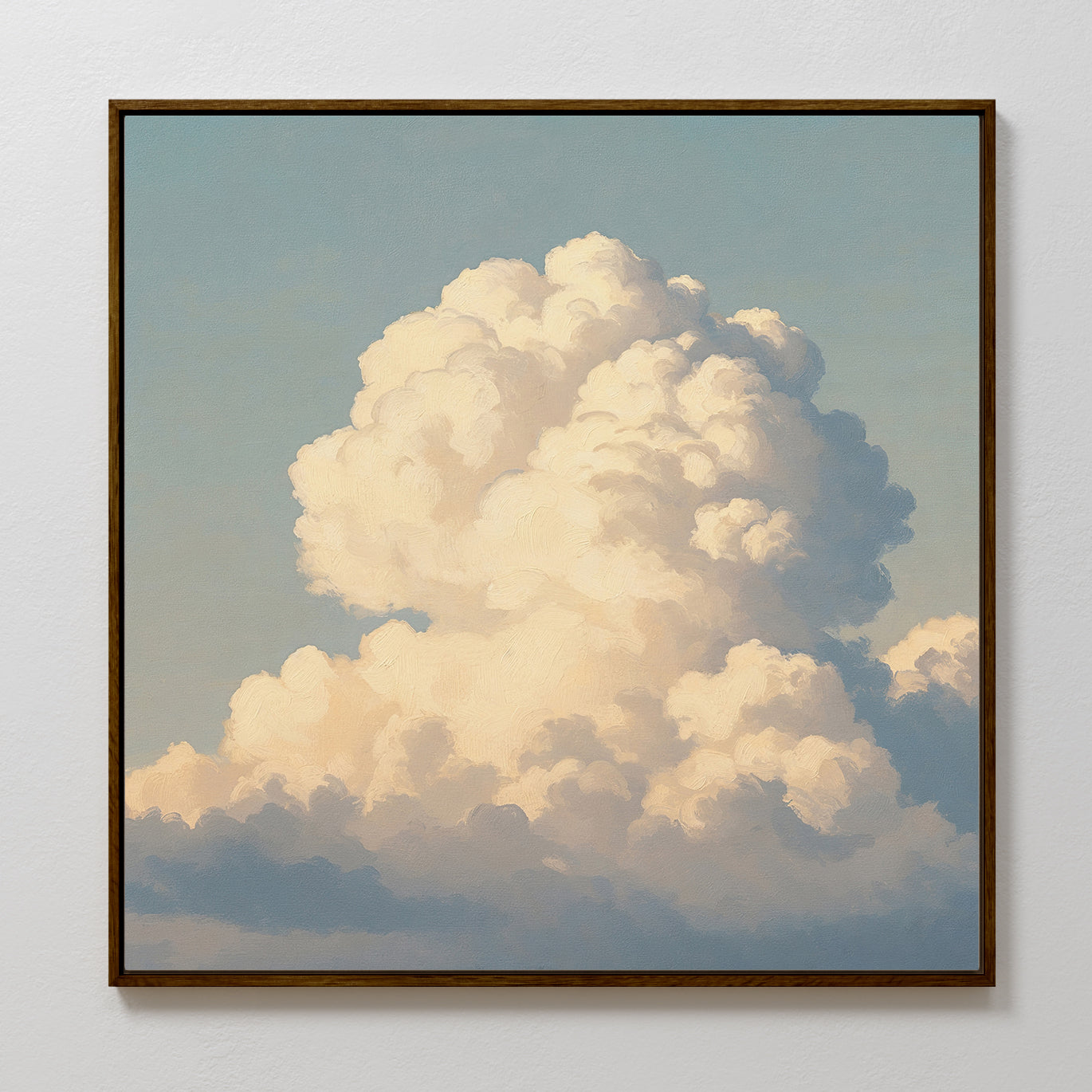 The Soft Skies Rising Canvas Art features a framed print of a fluffy white cloud against a blue sky on a white wall, highlighted by sunlight that casts soft golden tones and gentle shadows, bringing cloud-inspired beauty to any space.