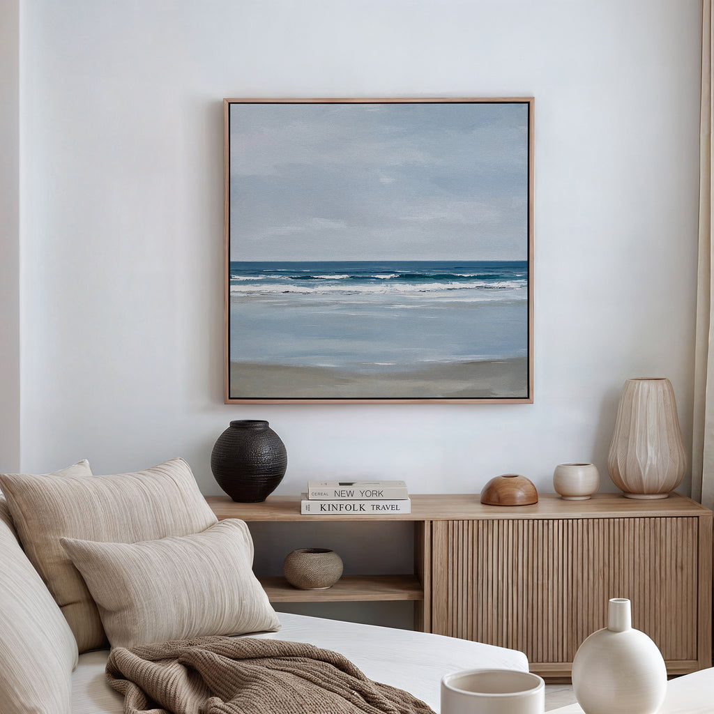 A serene living room with a beige sofa, neutral cushions, wooden sideboard with ceramic vases and books, plus coastal decor touches like the Soft Tide Canvas Art framed and hung on the white wall above.