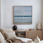 A serene living room with a beige sofa, neutral cushions, wooden sideboard with ceramic vases and books, plus coastal decor touches like the Soft Tide Canvas Art framed and hung on the white wall above.