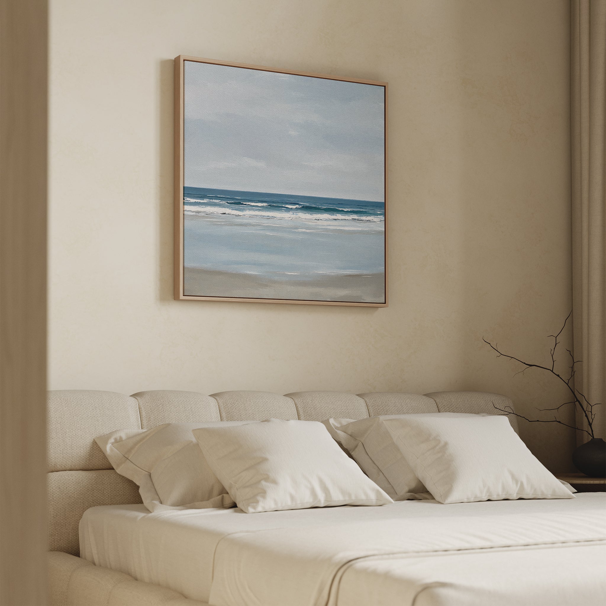 A cozy bedroom with a beige upholstered bed and white pillows, featuring coastal decor and the Soft Tide Canvas Art—a serene beach scene with blue sky and ocean waves—displayed above the headboard.