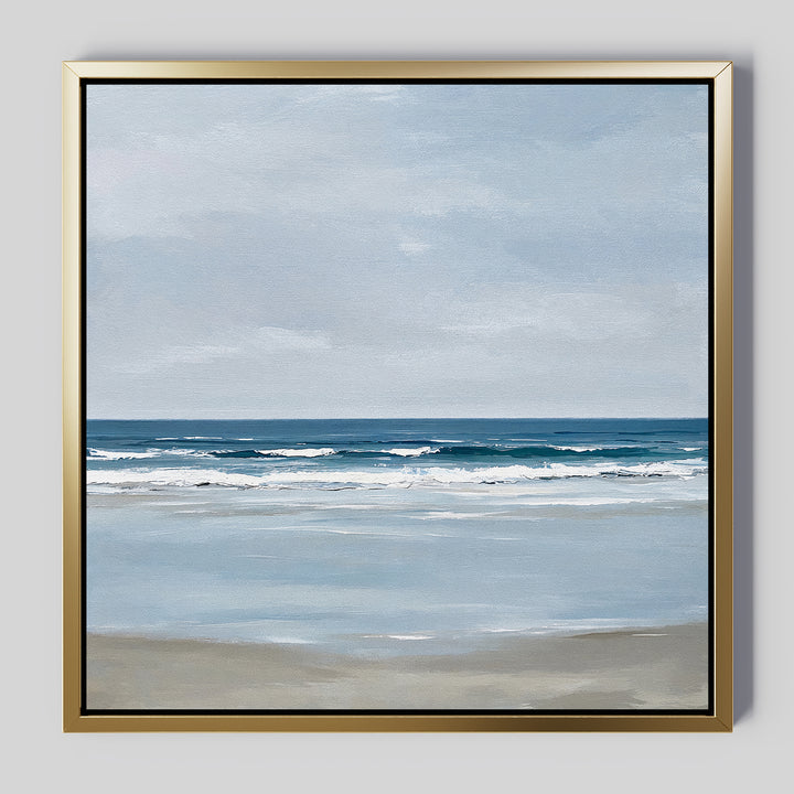The Soft Tide Canvas Art features a calm beach scene with gentle waves, a sandy shore, and a cloudy sky in soft blue and beige. It’s elegantly framed in gold with a black inner edge, making it perfect coastal decor for any space.