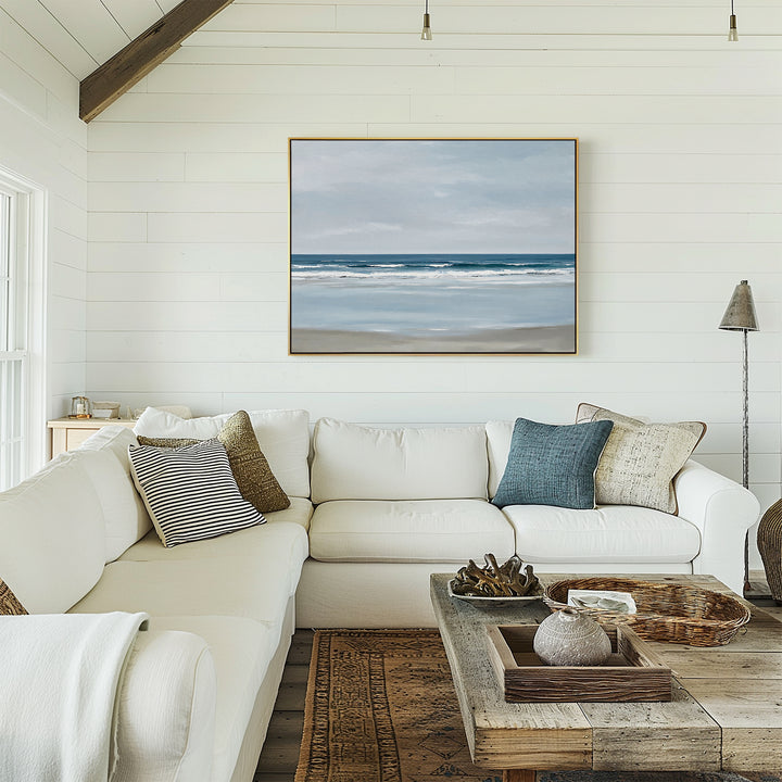 A cozy living room with white shiplap walls, a large beige sectional with assorted pillows, a rustic wood coffee table, and Soft Tide Canvas Art – Horizontal hanging above the couch.